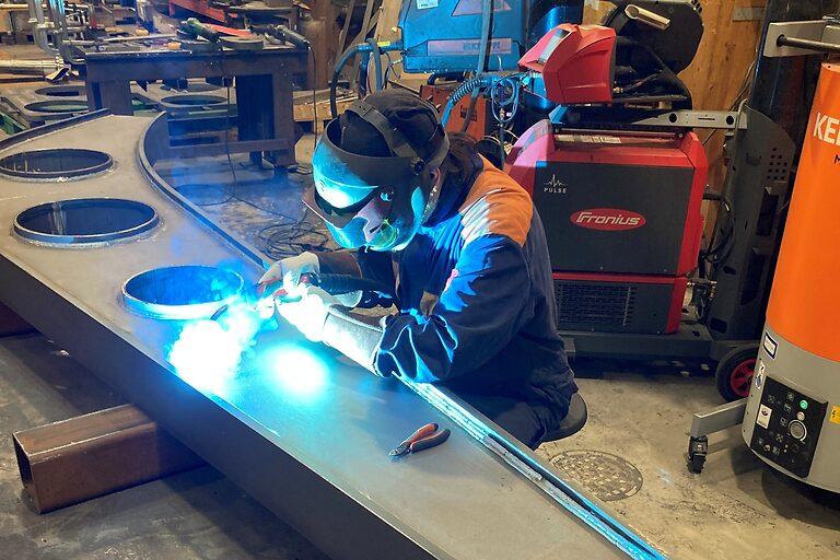 Welder welding a steel lifting accessory in a machine shop